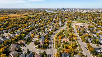 Aerial view of a Saskatoon neighbourhood with mature autumn trees and the city skyline in the distance