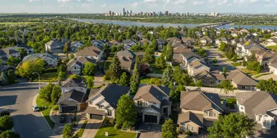 Aerial view of a Saskatoon suburban neighbourhood with family homes, trees and the downtown skyline across the river
