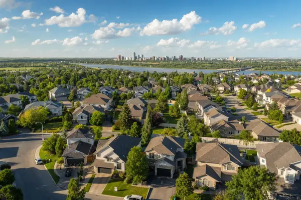 Saskatoon neighbourhood illustration with detached homes, leafy trees, a river and distant skyline