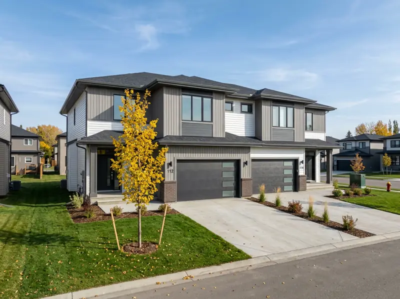 Newly built semi-detached two-storey homes with front garages and a young fall tree in Aspen Ridge