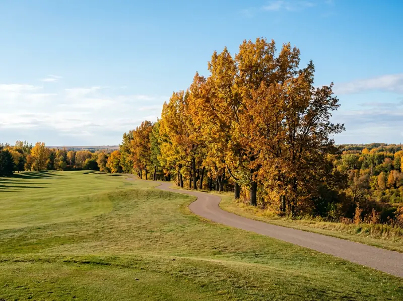 Golf course fairway lined with gold fall trees and a paved trail toward the river valley in Holiday Park