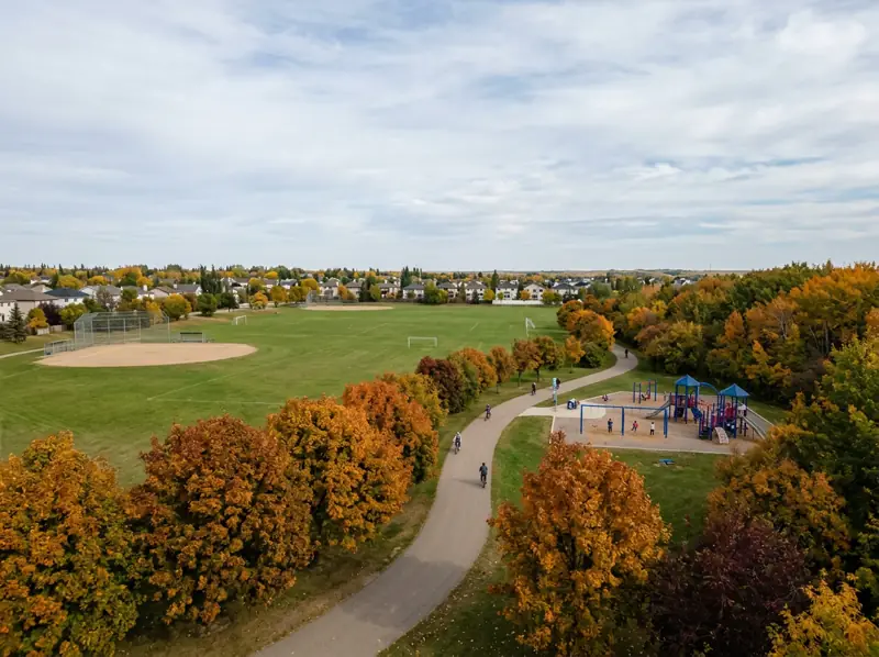 Open park sports fields, backstop and tree-lined path in fall colours in Hudson Bay Park, Saskatoon