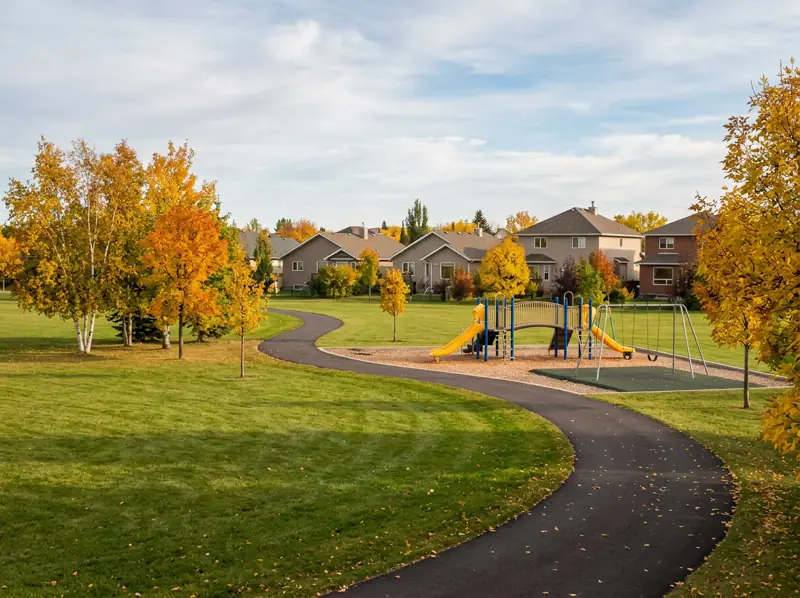 Neighbourhood park with a playground, open grass and a paved path under fall trees in Lakeridge