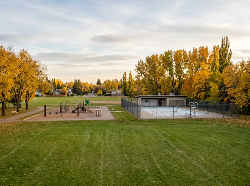 Mayfair Saskatoon park with sports field, playground and fenced outdoor pool under golden fall trees