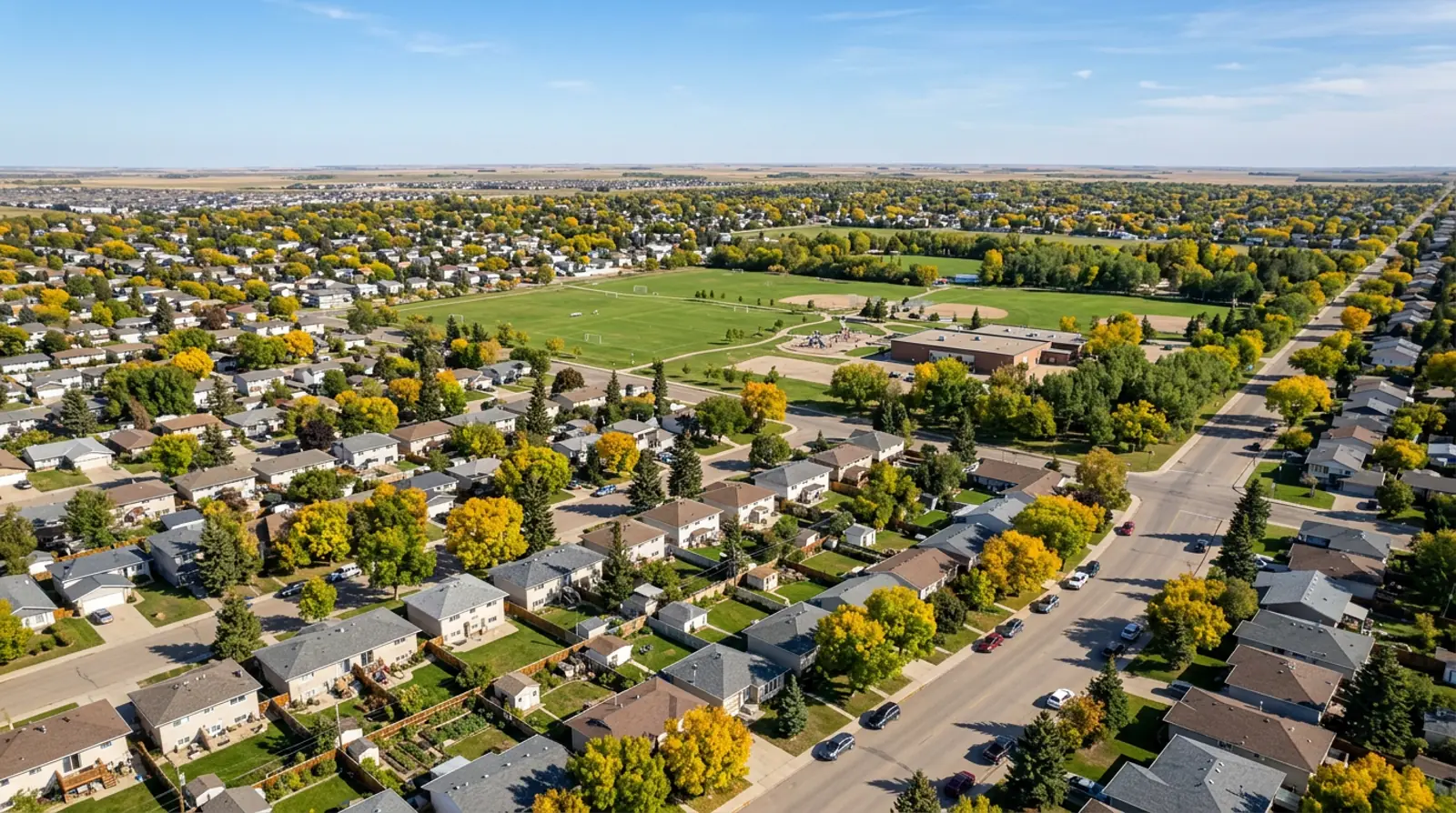 Aerial of Pacific Heights detached homes on wide lots beside a large park field in fall, Saskatoon
