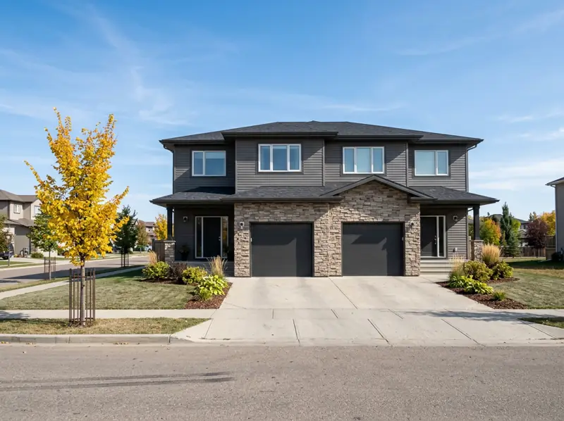 Modern semi-detached two-storey homes with attached garages and a young fall tree in Rosewood, Saskatoon