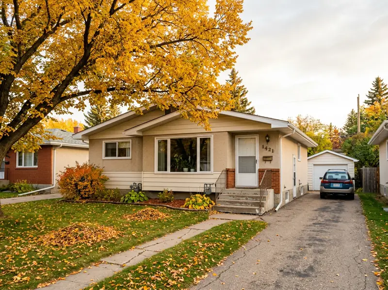 Modest 1960s stucco bungalow with a picture window and a gold fall tree in Sutherland, Saskatoon