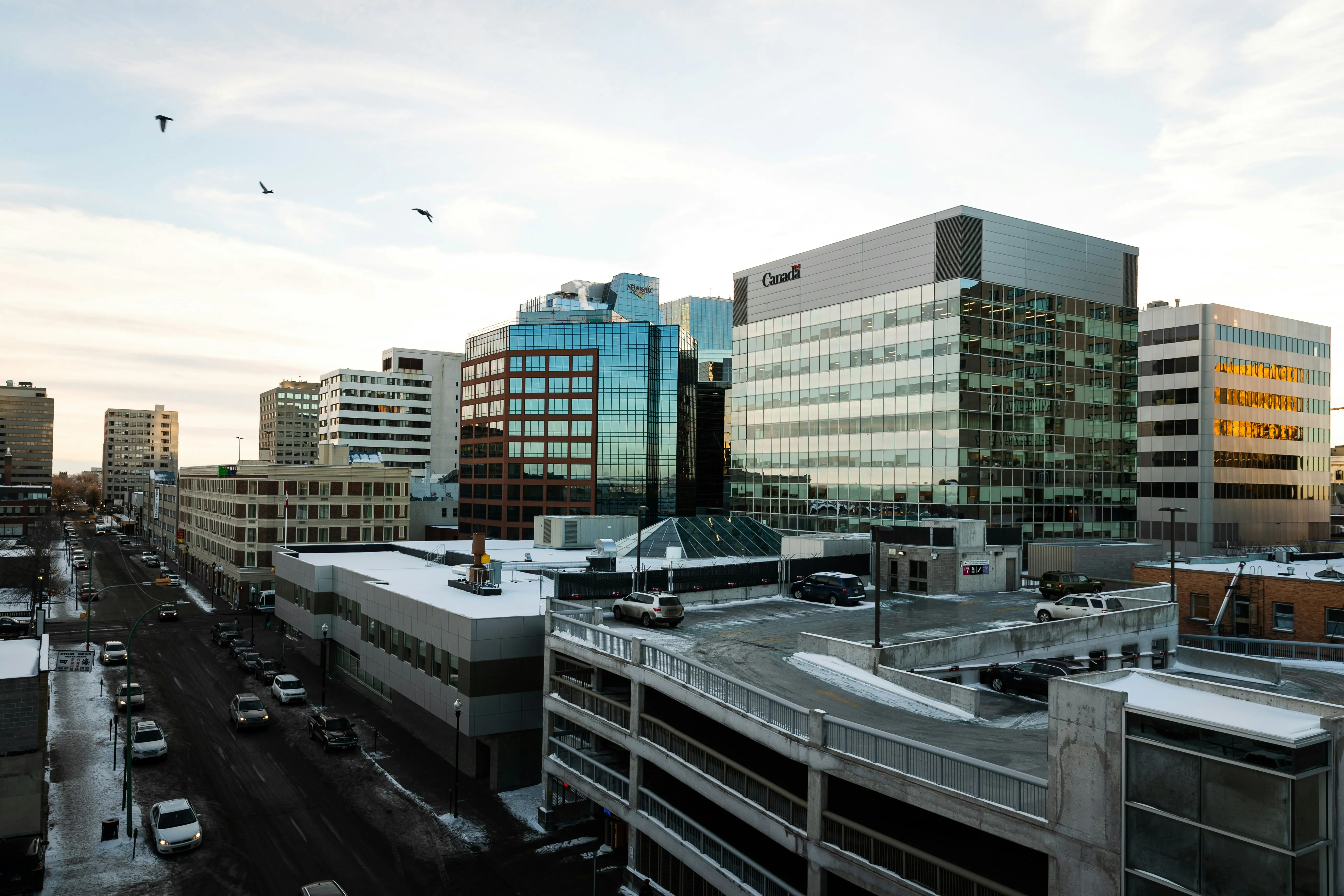 Downtown Regina Saskatchewan skyline showing modern office buildings, glass towers, and a parking structure on a winter morning.